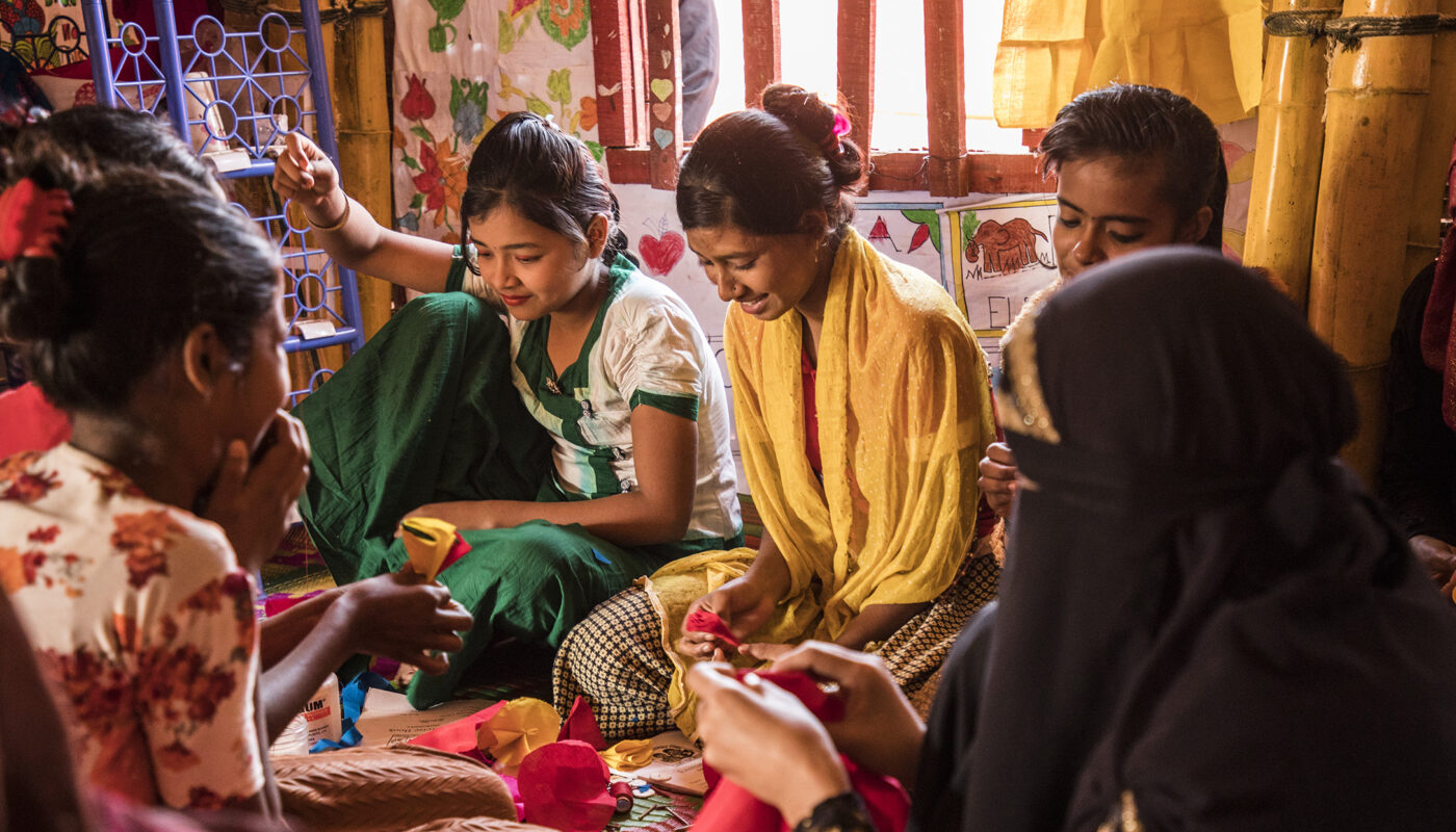 Adloescent girls laugh while making flowers at Naf Adolescent Club.
Camp 17, Kutupalong camp, Cox’s Bazar, Bangladesh. ; The ongoing Rohingya emergency is one of the biggest and most pressing crises of our time. In late August 2017, amidst unimaginable violence, hundreds of thousands of Rohingya left their homes in Rakhine State, Myanmar, and started their journey towards Bangladesh, in what quickly became the fastest growing refugee influx the world had seen in decades. 

An estimated 915 000 Rohingya lives in refugee camps in the area of Cox’s Bazar, Bangladesh. Half of the refugees (nearly 55%) are children under the age of 18 years.